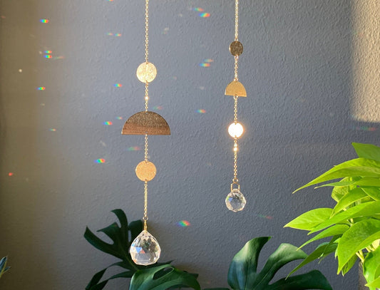 One small and one large brass and crystal suncatcher that disperse rainbow flecks around the walls and floor. A textured brass circle, semi circle and second circle suspended vertically. A round crystal prism hangs from the bottom.