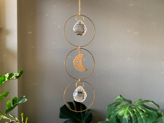 Brass and crystal suncatcher that disperses rainbow flecks around the walls and floor. Three brass hoops connected vertically Small round crystal inside the top and bottom hoop. A brass crescent moon with leaf cut outs in the center hoop.