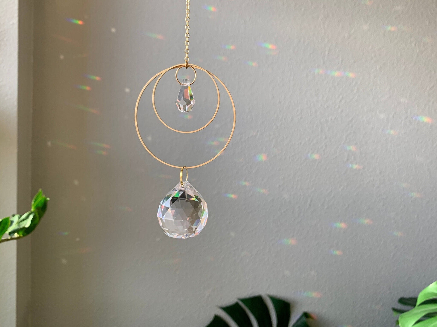 Brass and crystal suncatcher that disperses rainbow flecks around the walls and floor. Two brass hoops layered, one small and one large. Small teardrop crystal inside the small hoop. A larger round crystal ball hangs below the large hoop.