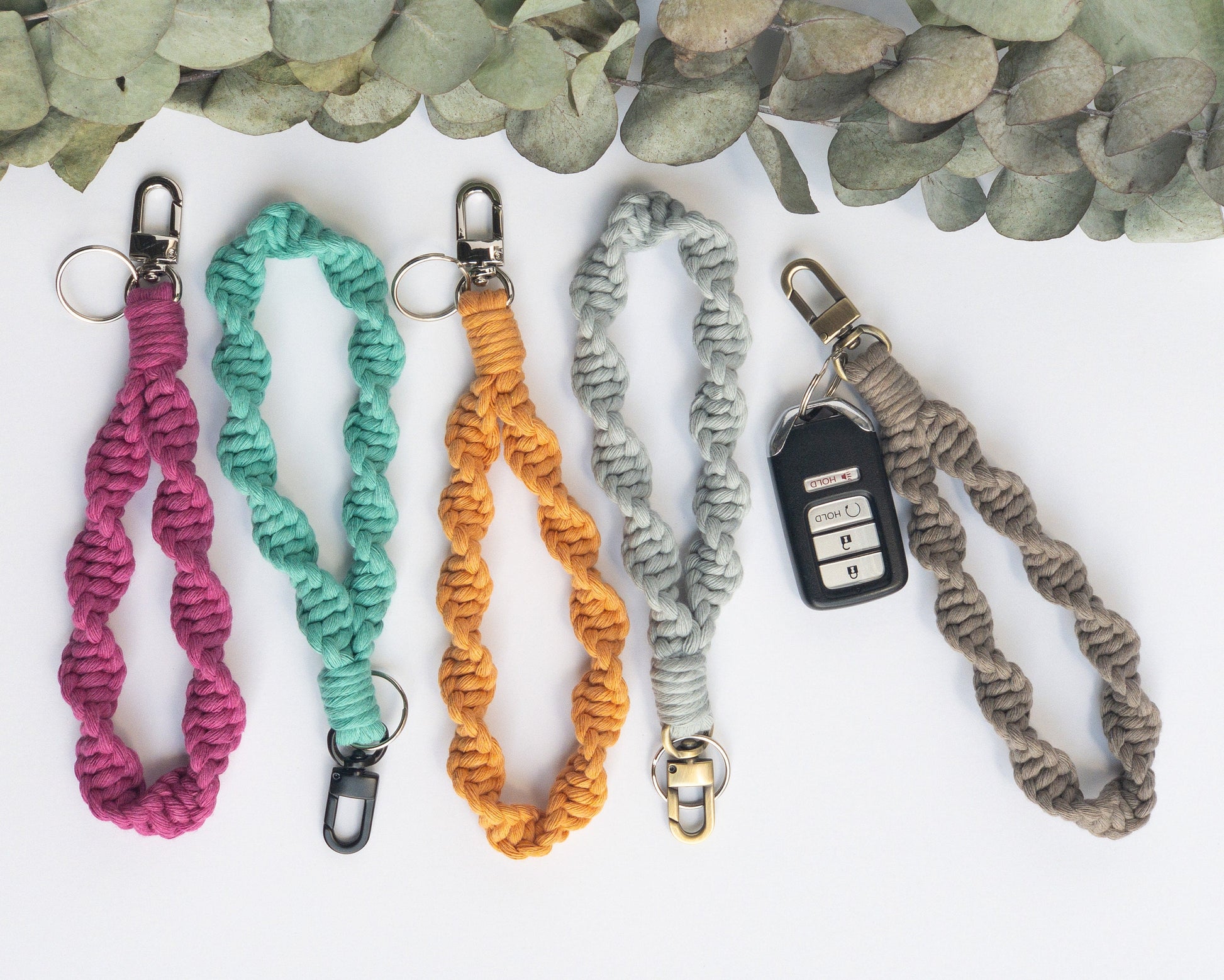 Wristlet Style Macrame keychain in a twisted spiral pattern. Shown in 5 colors, hot pink, aqua, yellow, light blue and taupe. Brass, silver and smoke colored hardware. Keyfob shown on taupe keychain.