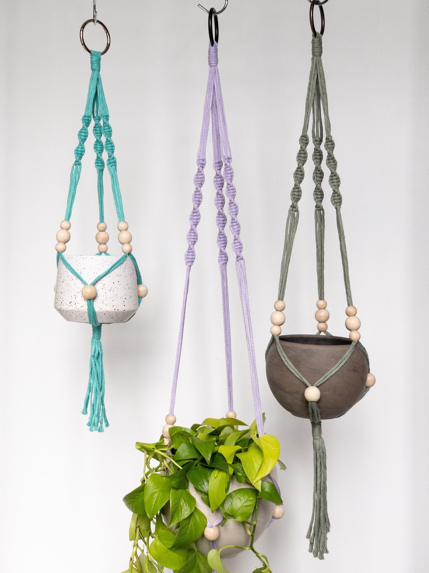 Three macrame plant hangers, lavender, aqua and green. Each have 3 spiral straps to hold the pots. Each strap has 3 moveable beads that sit just above the pot. Another moveable bead sits at the center of the pot. They have tassels at the bottom.