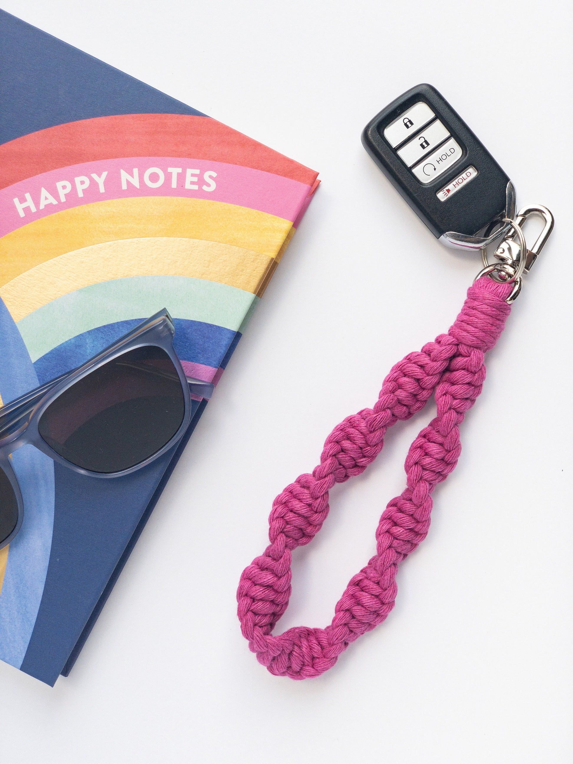 Wristlet Style hot pink Macrame keychain in a twisted spiral pattern with key fob attached. Styled with a notebook and sunglasses.