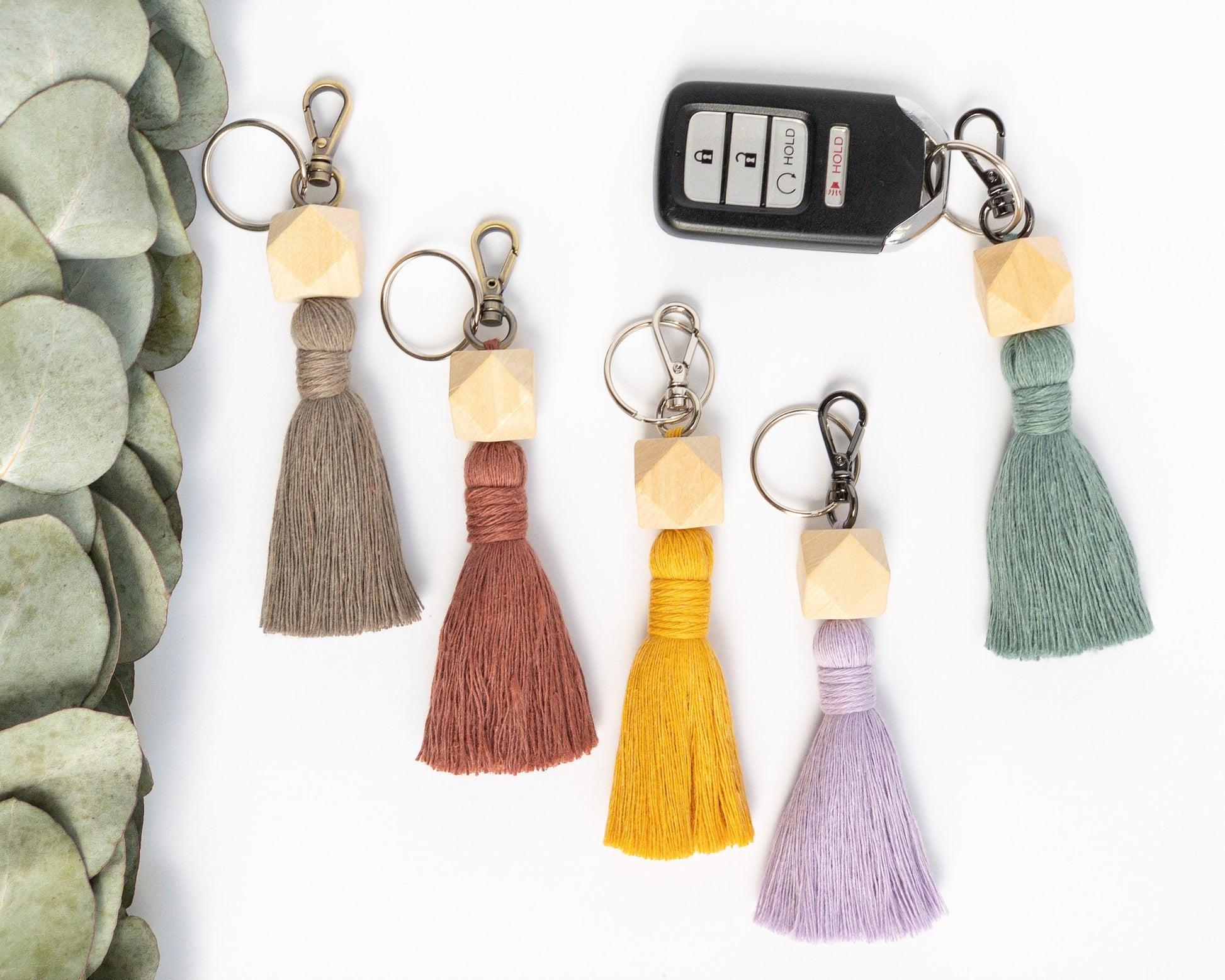 Macrame keychain shown in 5 colors. Brass, silver and smoke colored hardware. 3 dimensional hexagon wood bead at the top with a colored tassel below the beads. Keyfob shown on one keychain. Rosewood, Teal, Yellow, Lavender, Taupe examples.