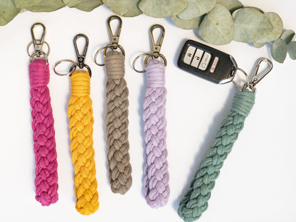 Wristlet Style Macrame keychain in a braided pattern. Shown in 5 colors, hot pink, yellow, taupe, lavender and teal. Brass, silver and smoke colored hardware. Keyfob attached to teal keychain.