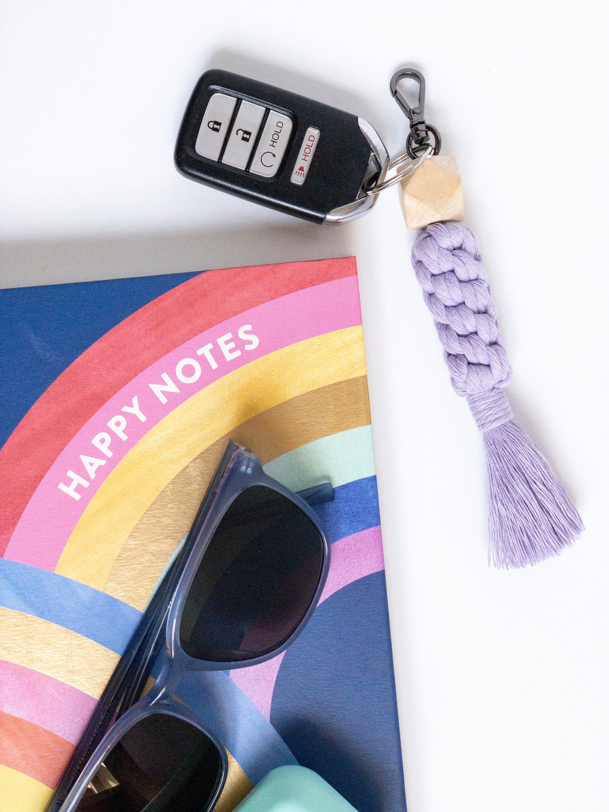 lavender macarame keychain with keyfob attached. 3 dimensional hexagon wood bead and smoke gray hardware. Styled with sunglasses and notebook