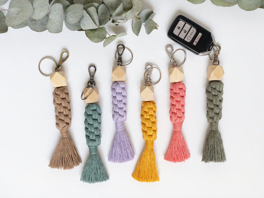 Macrame keychain shown in 6 colors. Brass, silver and smoke colored hardware. Three dimensional hexagon wood bead at the top. small brushed tail at the bottom. Keyfob shown on one keychain. Brown, Teal, lavender, yellow, coral and green examples.