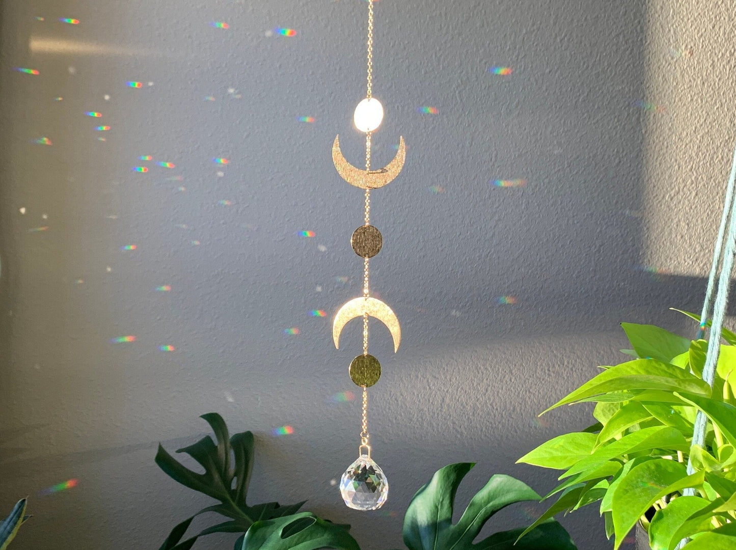 Brass and crystal suncatcher that disperses rainbow flecks around the walls and floor. Textured brass pieces representing the phases of the moon. Two crescent moon shapes and three round. A large round crystal ball hangs from the bottom.