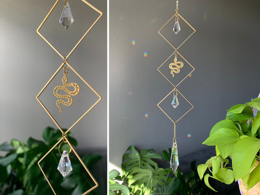 Brass & crystal suncatcher disperses rainbow flecks on the wall. 3 brass diamonds connected vertically, a small crystal icicle inside the top & bottom diamond. Center diamond has brass snake. A larger icicle crystal hangs below the bottom diamond.